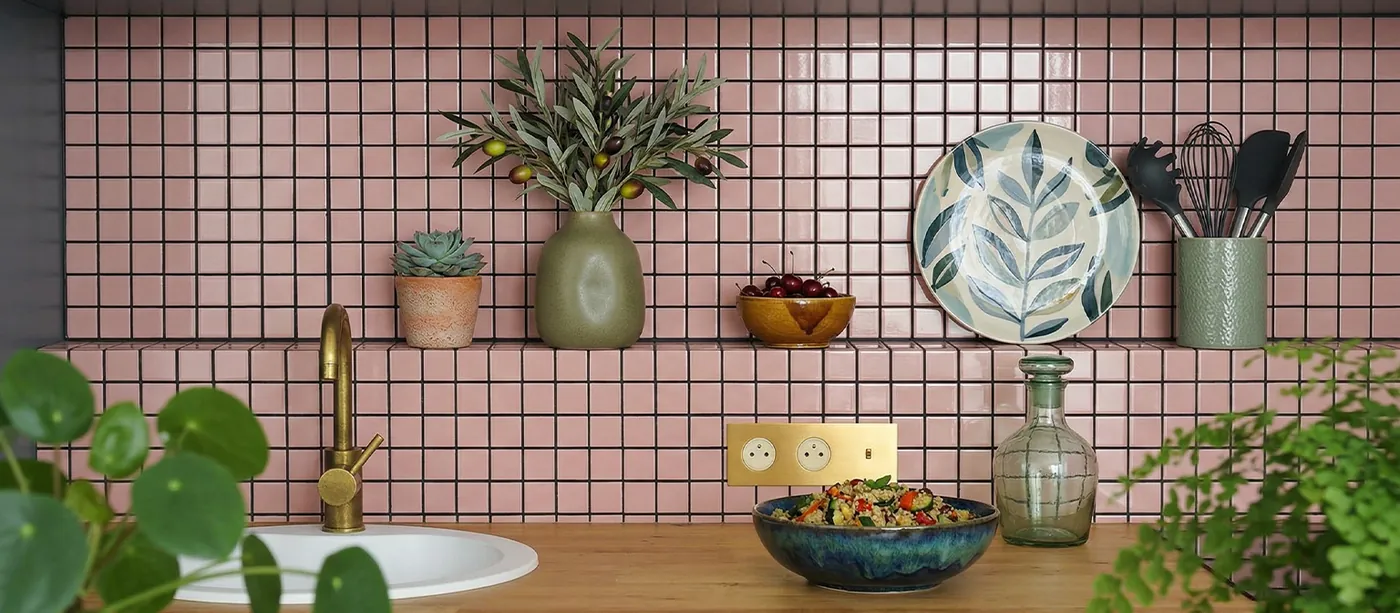 Cocina con frente de mosaico cerámico rosa, grifería dorada y plantas